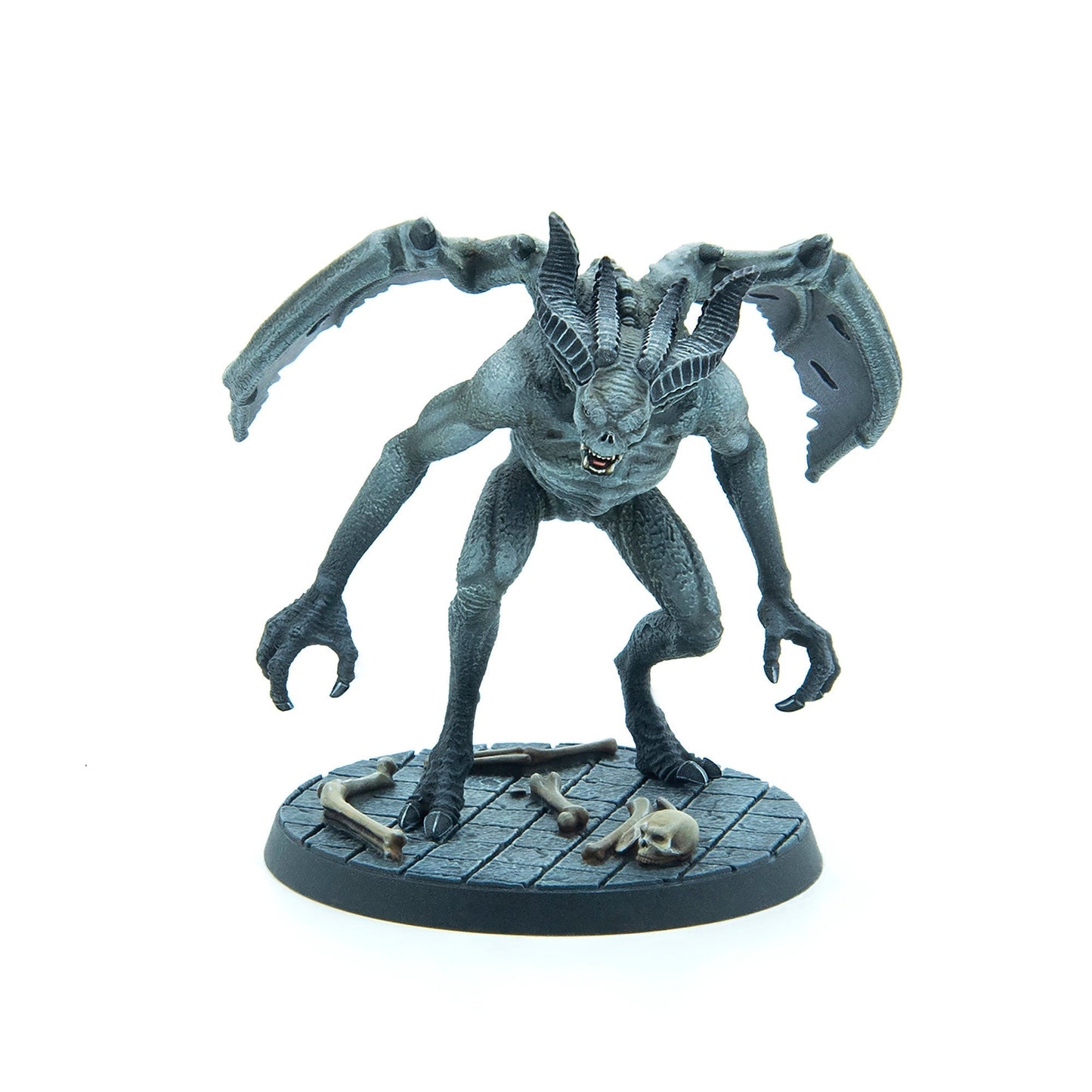 Grey winged monster figurine with horns, fangs, and claws, standing on a dark base with bones and a skull