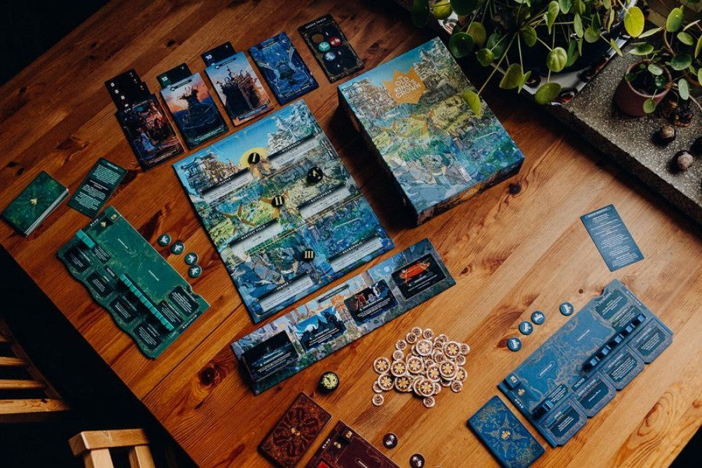 Components for a complex fantasy board game, including map boards, cards and tokens, spread on a wooden table