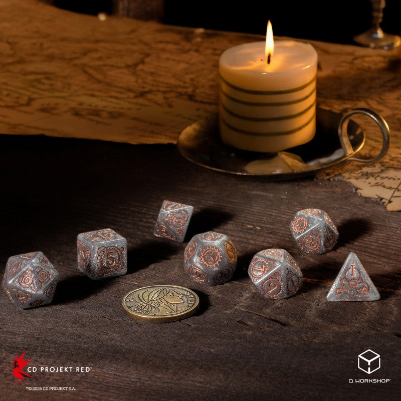 Seven grey and copper dice with gear designs and a brass coin on a dark wood table, with a lit candle and map