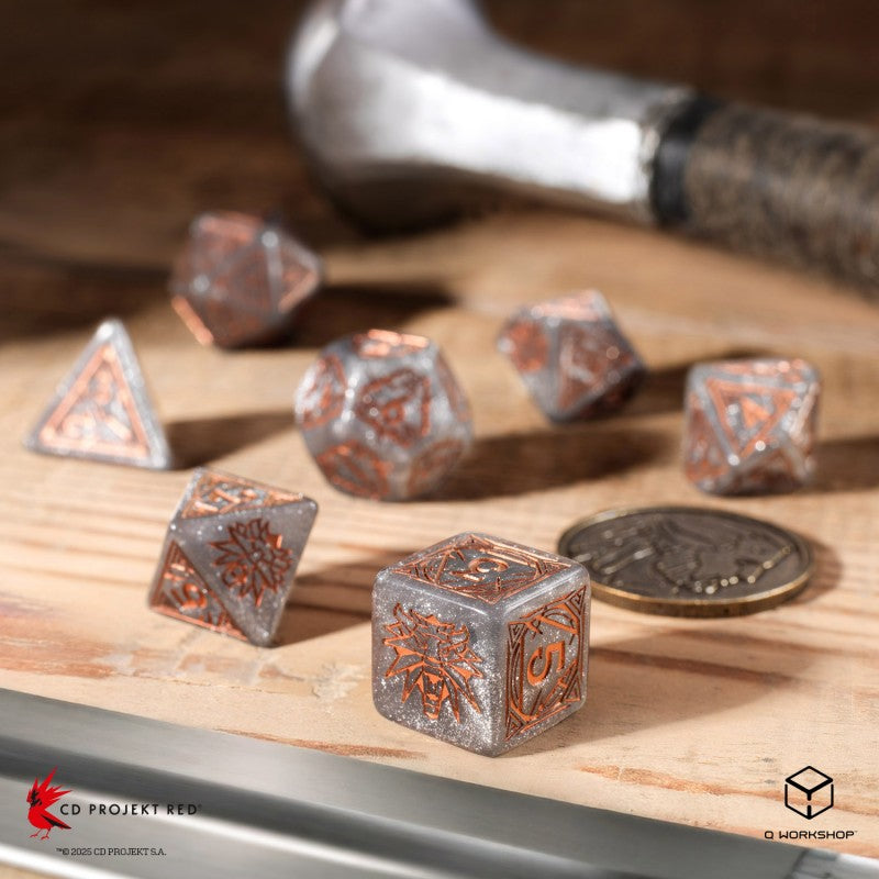 Sparkly gray and copper Witcher dice on a wooden table, with a blurred hammer and coin