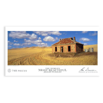 Puzzle shows abandoned stone farmhouse with rusty roof in a vast, dry golden field under a blue sky