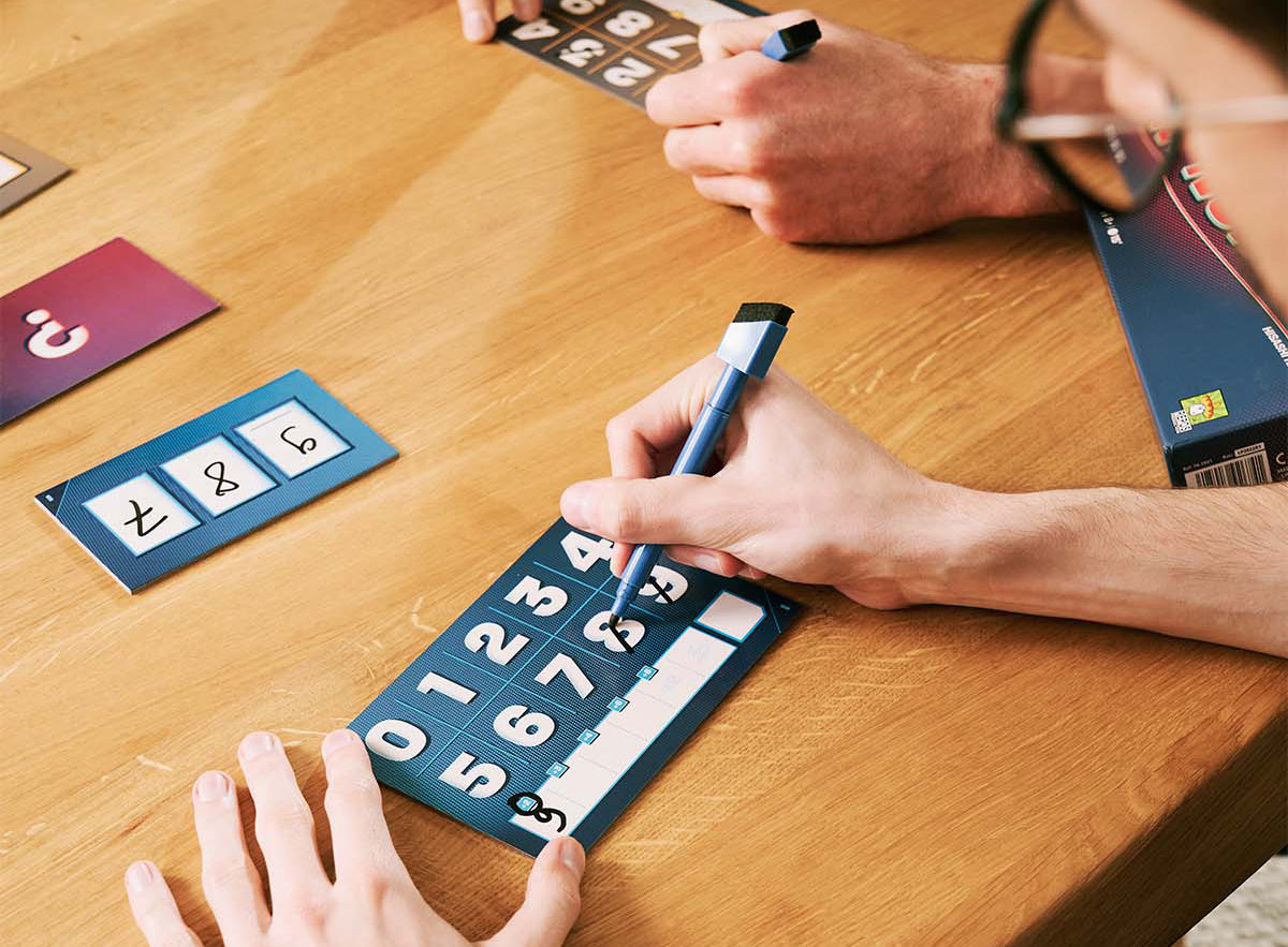 Lifestyle photo showing a group of people playing The Number Game at a table with cards and scorepad visible
