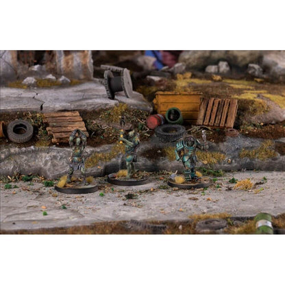 Three ghoulish miniatures with axes and weapons stand on a textured post-apocalyptic diorama with rubble