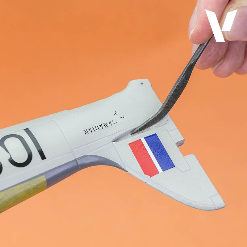A hand files a grey model airplane, detailed with red and blue stripes