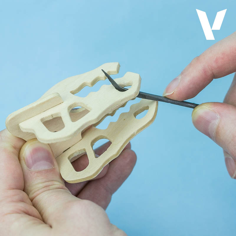 Hands file the notched edges of two light wooden pieces with a small metal file