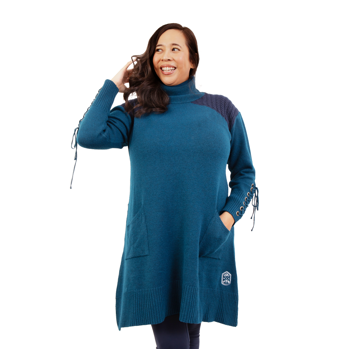 Smiling woman in a teal turtleneck sweater dress with laced sleeves, hands in hair and pocket