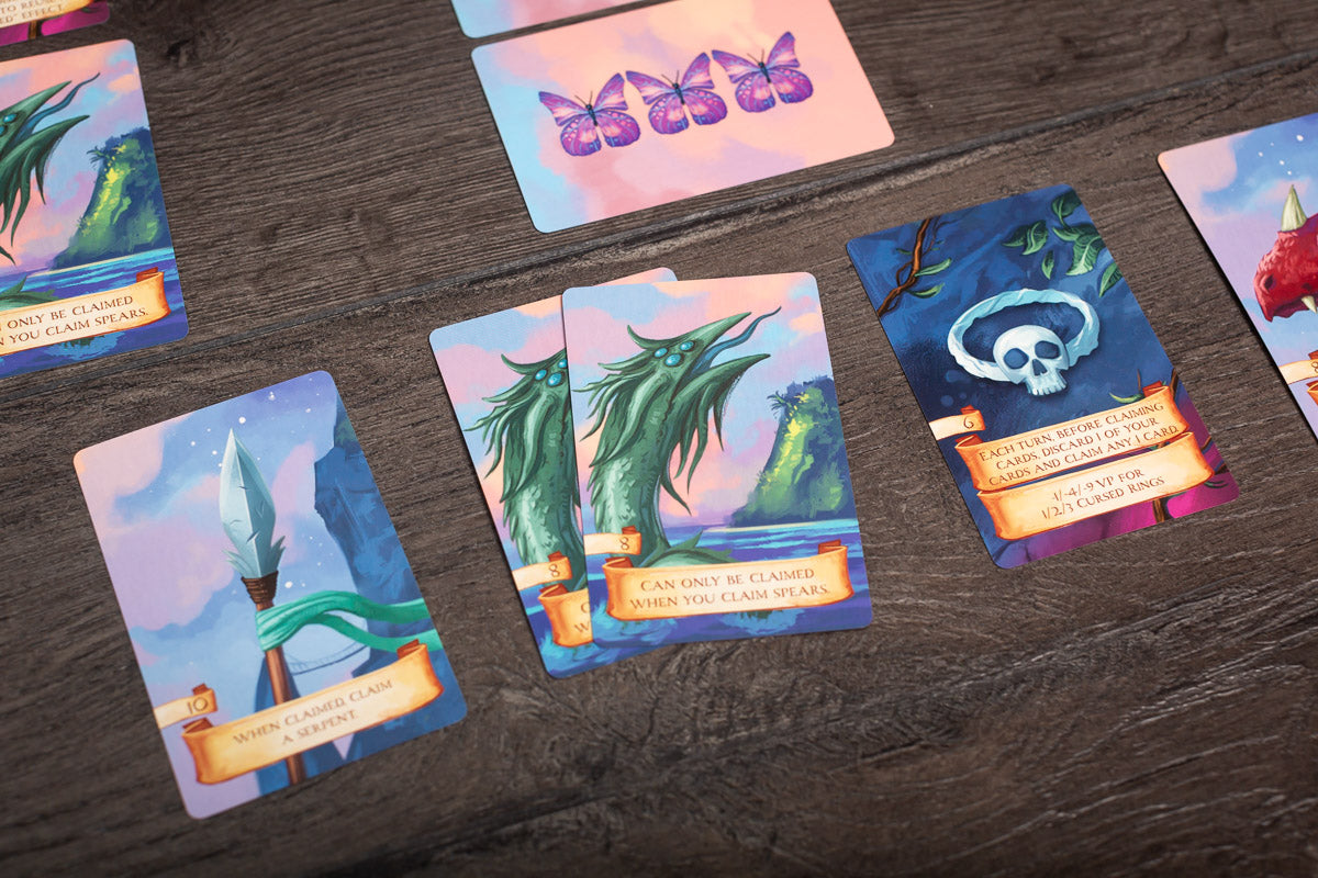 A photo showing a player holding cards while playing Isle of Night, with the game board and pieces visible in the background