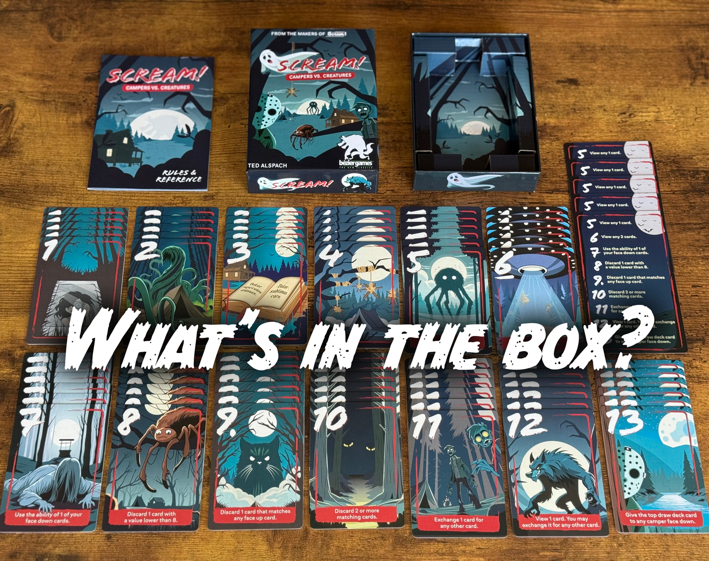 Scream! Campers vs. Creatures game components laid out on wood, box, rulebook, and numerous horror creature-themed cards