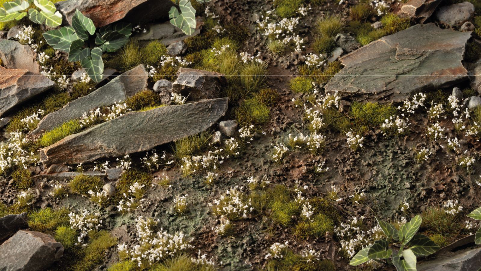 Detailed miniature terrain featuring slate rocks, grass tufts, white flowers, and green leaves
