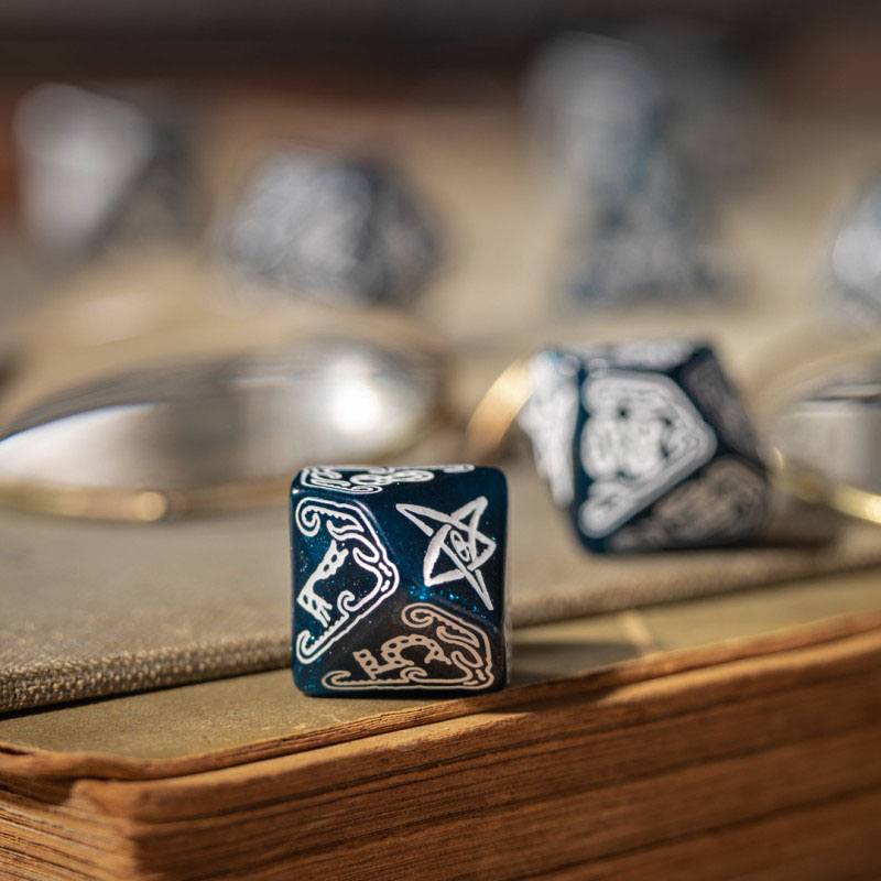Blue speckled dice displaying white Norse-style artwork of a horse a star and an intertwined pattern resting on an old book
