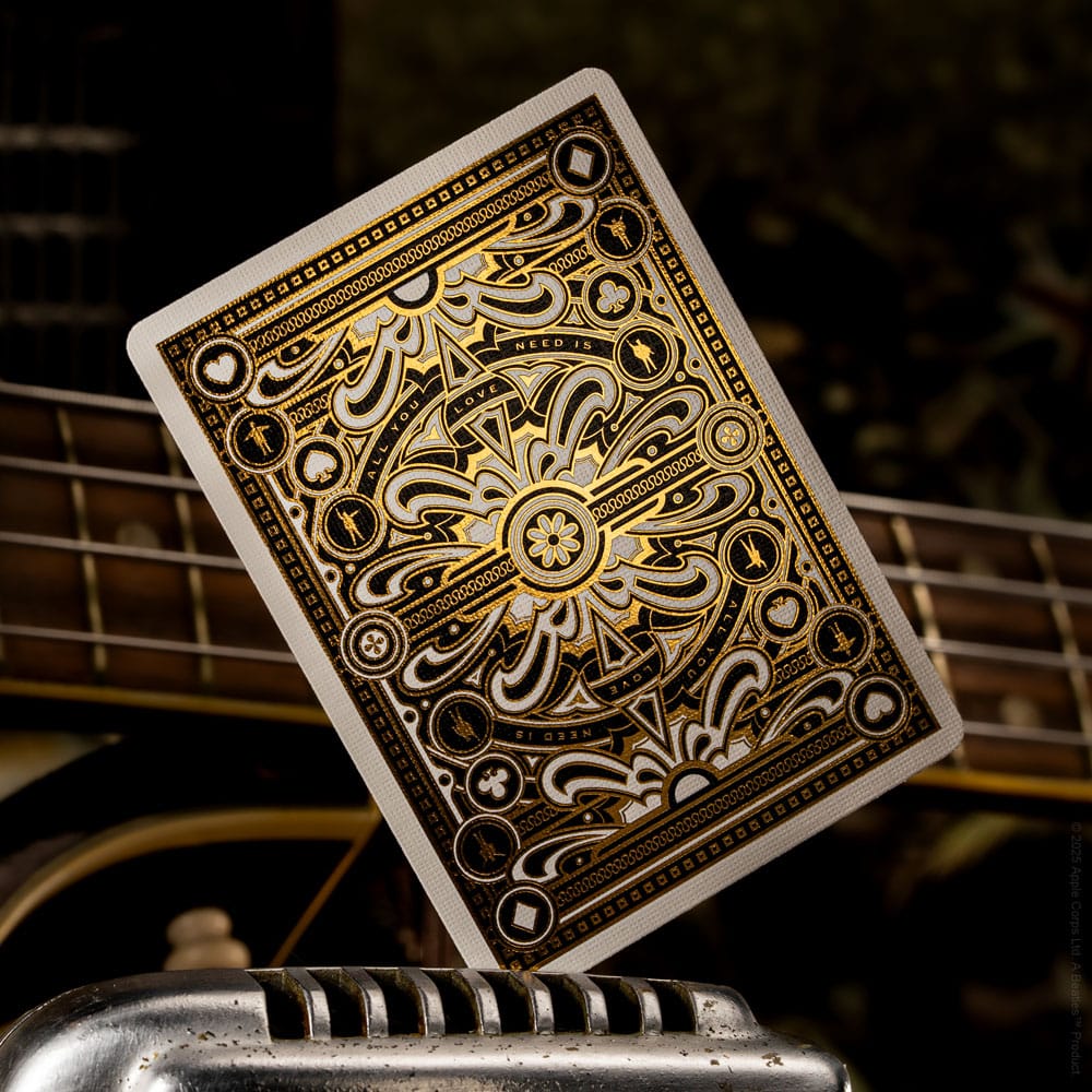 Ornate black and gold custom playing card back displayed over guitar strings and a chrome object
