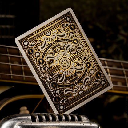 Ornate black and gold custom playing card back displayed over guitar strings and a chrome object